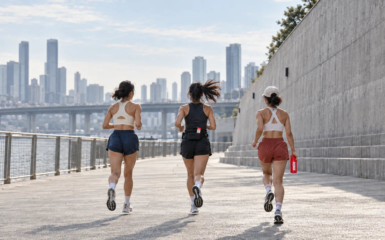 Three runners on a waterfront path, one carrying a red XALT bottle