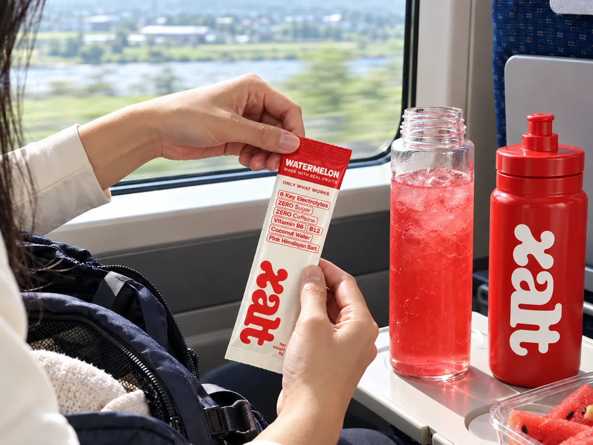 Opening a Watermelon sachet on a train, with a drink and a red XALT bottle on the table