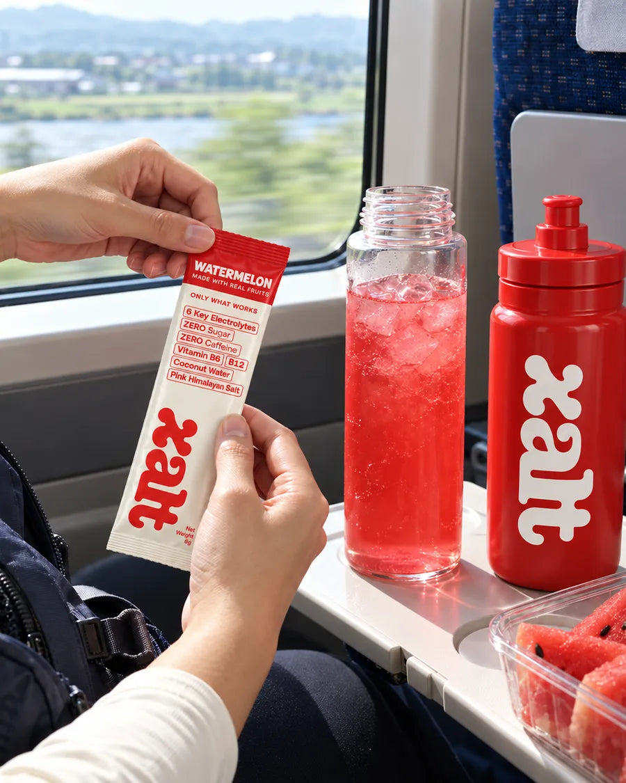 Opening a Watermelon sachet on a train, with a drink and a red XALT bottle on the table